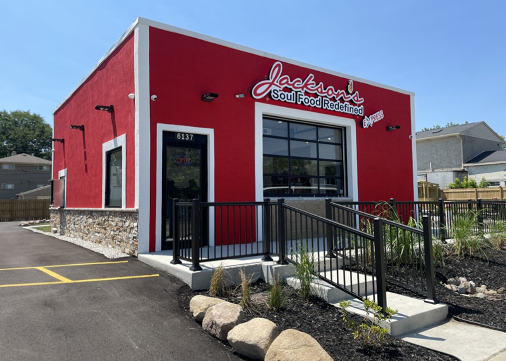 Bright red restaurant with a modern design, labeled "Jackson's Soul Food Redefined" at the entrance. Black railing and fresh landscaping in front.
