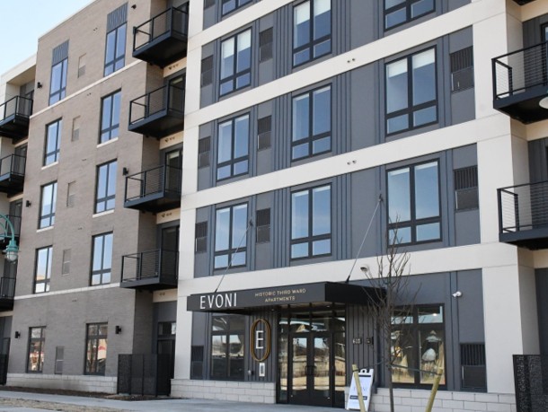 Four-story modern apartment building with large windows and balconies, gray and beige facade. Sign above entrance reads "EVONI," conveying a contemporary feel.