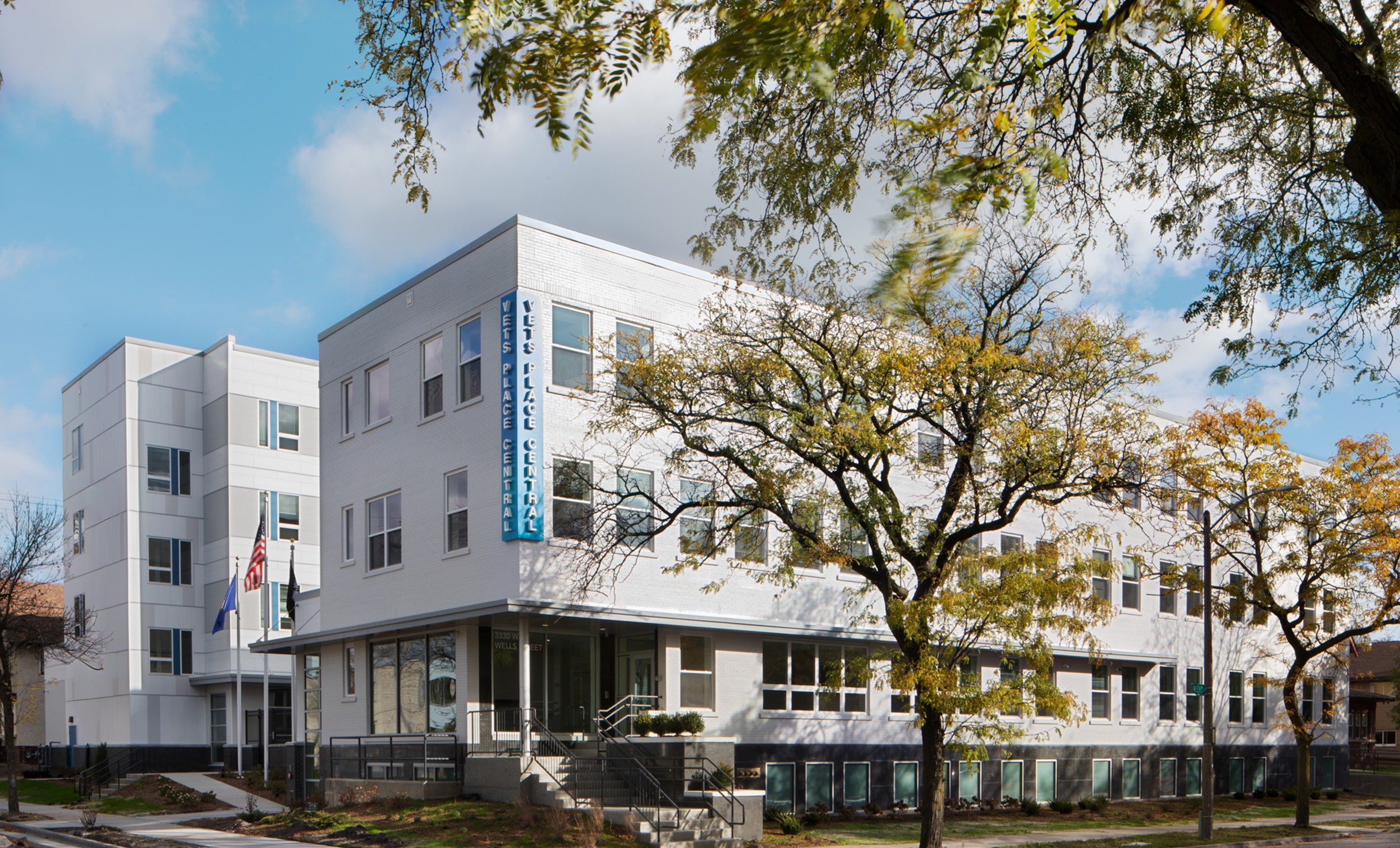 A modern, white, three-story building with a blue vertical sign stands amid trees on a sunny day, conveying a professional and welcoming atmosphere.