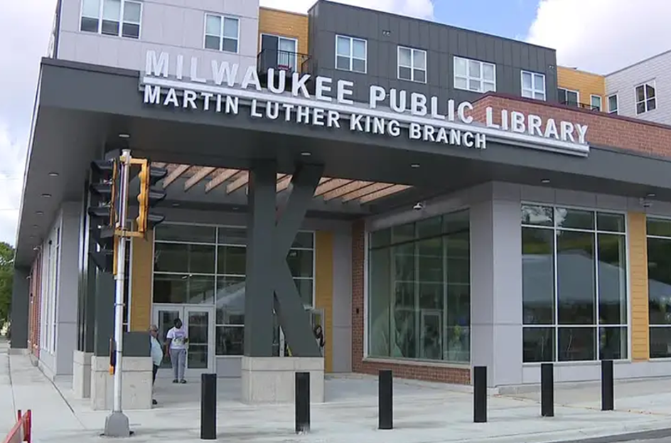 Front view of Milwaukee Public Library, Martin Luther King Branch. Modern exterior with large windows, a sign, a traffic light, and people near the entrance.