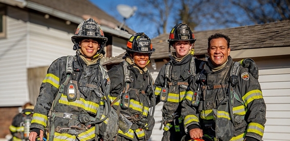 Four Milwaukee Fire Department recruits posing for a photo in the golden hour sunlight in front of a vacant house