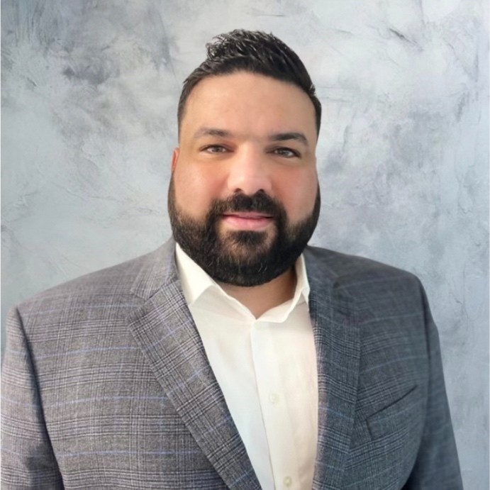 Man with black hair smiles with gray suit and white dress shirt